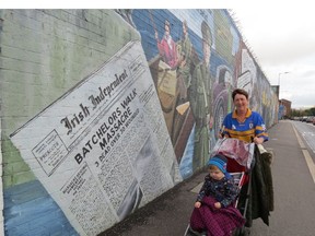 A mother pushes a stroller past one of the many murals in Belfast that document historical events in Northern Ireland history.