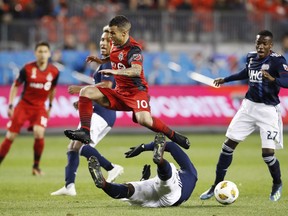 Toronto FC's Sebastian Giovinco jumps over New England Revolution's Jalil Anibaba, bottom, and as Luis Caicedo, right, looks on during the first half of MLS soccer action in Toronto, Saturday September 29, 2018.