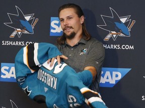 Newly acquired San Jose Sharks defenseman Erik Karlsson puts on jersey during a news conference held by the NHL hockey team in San Jose, Calif., Wednesday, Sept. 19, 2018.