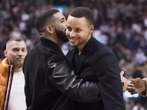Rapper Drake (left) hugs Warriors guard Stephen Curry during the first half at Scotiabank Arena last night. Curry hasn’t played since injuring his left groin on Nov. 8. Nathan Denette/CP