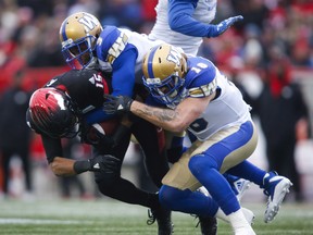 Blue Bombers’ Kevin Fogg (centre) and Taylor Loffler (right) tackle the Stampeders’ Eric Rogers on Sunday. Rogers caught three touchdowns in the game. (The Canadian Press)