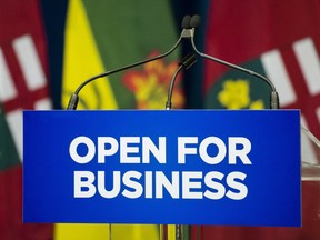 A sign with the slogan "Open for Business" is placed in front of a podium with the Ontario and Saskatchewan flags in the background in Queen's Park in Toronto on Monday, October 29, 2018.