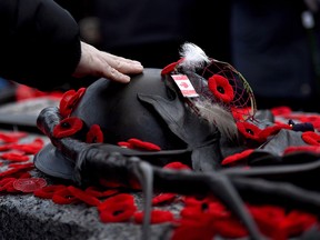 A man touches the helmet on the Tomb of the Unknown Soldier after laying a poppy following the National Remembrance Day Ceremony at the National War Memorial in Ottawa on Saturday, Nov. 11, 2017.