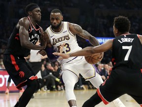 Los Angeles Lakers' LeBron James (23) dribbles between Toronto Raptors' Pascal Siakam, left, and Kyle Lowry (7) during the first half in Los Angeles on Sunday. (AP Photo/Marcio Jose Sanchez) LAS106