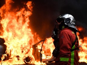 A firefighter stands in front of vehicles set on fire during a protest against rising costs of living, on the Champs-Elysees in Paris on Saturday, Dec. 8, 2018.