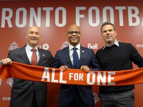 From left, Toronto FC president Bill Manning, new general manager Ali Curtis and head coach Greg Vanney hold up a team scarf at a news conference introducing Curtis on Thursday. (THE CANADIAN PRESS)