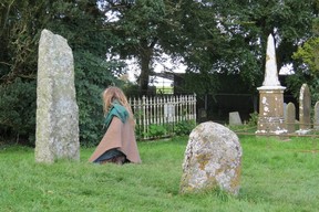 Member of cult prays in front of remains of cross near Hill of Tara. The stone surface has a worn “Sheelagh Na Gig” fertility symbol. (Ian Robertson photo)