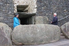 Visitor and guide to Newgrange monument behind entrance stone engraved with megalithic art. (Ian Robertson photo)