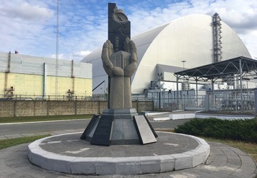 A memorial to those who fought to contain the damage caused by the 1986 Chornobyl nuclear disaster, many of whom gave their lives, is located steps from Reactor number 4 — seen in the background covered by a massive steel and concrete sarcophagus. (Chris Doucette/Toronto Sun/Postmedia Network)