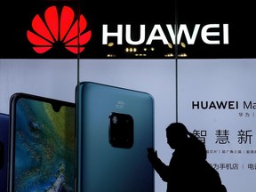In this Dec. 11, 2018, file photo, a woman browses her smartphone as she walks by a Huawei store at a shopping mall in Beijing.