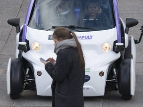 A woman uses a mobile phone as she walks in front of an autonomous self-driving vehicle, as it is tested in a pedestrianised zone, during a media event in Milton Keynes, north of London, on October 11, 2016. (AFP Photo)
