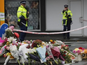 Flower rest at a road block while two police officers stand guard next to the makeshift memorial near the Linwood mosque in Christchurch, New Zealand, on Saturday, March 16, 2019. (AP Photo/Vincent Thian)