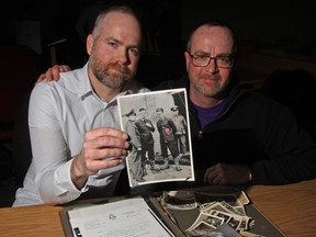 Thompson’s grandson, Jesse Beauchamp (left) and Thompson’s son, Andrew Thompson, (right) show a faded 75-year-old German propaganda photo of Thompson (third from the left) with hands tied behind his back after he was captured by the Germans when his plane crashed.