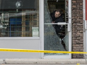 A Toronto police officer peers through the shattered glass door of a variety store on Jane St. after a Tuesday morning shootout.