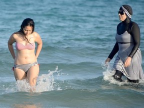 Two Tunisian women, one wearing a "burkini", a full-body swimsuit designed for Muslim women, walking in the water at Ghar El Melh beach near Bizerte, north-east of the capital Tunis.