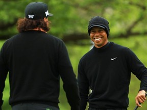 Tiger Woods (R) of the United States smiles with Pat Perez (L) of the United States on the practice green during a practice round prior to the 2019 PGA Championship at the Bethpage Black course on May 14, 2019 in Bethpage, New York.