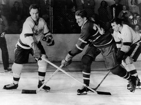Canadian hockey player Red Kelly (left) of the Detroit Red Wings battles with Paul Masnick of the Montreal Canadiens for an airborne puck while Red Wing Marty Pavelich (right) skates in to join the action during the final game of the Stanley Cup in Detroit, Michigan, April 16, 1954. Detroit went on to win the game and the Cup.