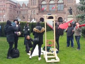 May Day protesters poses with signs, Communist flags and guillotine at Queen's Park on Wednesday, May 1 2019.