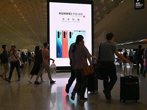 In this picture taken on May 30, 2019, people walk past Huawei advertising at Shenzhen-Bao'an international airport in Shenzhen, China's Guangdong province. - China on May 30 accused the United States of repeatedly lying about the effects of the trade war on its economy as Beijing prepares to hike tariffs on American goods ranging from wine to pianos and condoms.