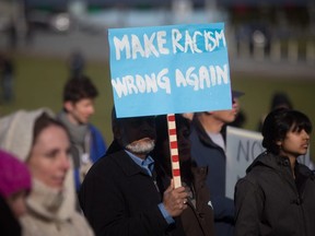 A man holds a sign reading 'Make Racism Wrong Again' during a 'No Wall, No Ban' rally at the Peace Arch-Douglas border crossing between Canada and the U.S., in Surrey, B.C., on Feb. 12, 2017.