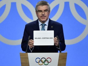 International Olympic Committee (IOC) president Thomas Bach shows the card with the name Milan/Cortina d'Ampezzo as the winning name of the 2026 Winter Olympics during the 134th session of the International Olympic Committee (IOC), in Lausanne on June 24, 2019.