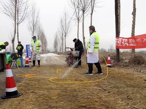 Police officers and workers in protective suits are seen at a checkpoint on a road leading to a farm owned by Hebei Dawu Group where African swine fever was detected, in Xushui district of Baoding, Hebei province, China February 26, 2019. (REUTERS/Hallie Gu)