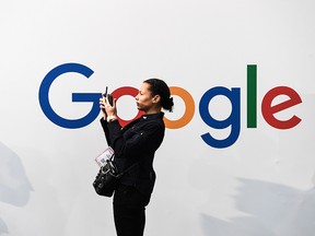 A woman takes a picture with two smartphones in front of the logo of the U.S. multinational technology and Internet-related services company Google.