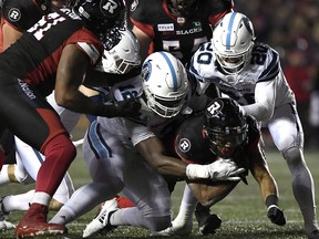 Argonauts linebacker Nelkas Kwemo (12) tries to bring down Redblacks running back Mossis Madu Jr. Justin Tangtthe Canadian Press