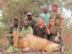 Jacques and Martine Alboud pose with their safari hunting group and the corpse of what appears to be a hartebeest.