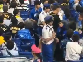 A video posted on Twitter shows a dad reportedly throwing his child at at a a man as he was being escorted out of a stadium in Yokohama, Japan on Tuesday. (@renna_shinohara/Twitter screengrab)