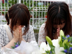 Women pray in front of bouquets placed for victims of the torched Kyoto Animation building in Kyoto, Japan, July 20, 2019. (REUTERS/Kim Kyung-Hoon)