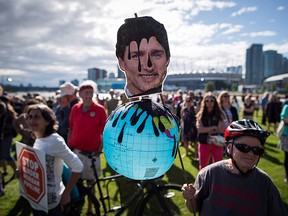 A protester holds a photo of Prime Minister Justin Trudeau and a representation of the globe covered in oil during a protest against the Kinder Morgan Trans Mountain Pipeline expansion in Vancouver, B.C., on Tuesday May 29, 2018.