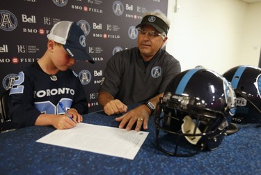 Darius Raso, a seven-year-old boy from Kleinburg, Ont. who has been battling acute lymphocytic leukemia for the past year, signs a one-day contract with the Toronto Argonauts as the CFL team's General Manager Jim Popp looks on Thursday, Aug. 29, 2019. (Jack Boland/Toronto Sun/Postmedia Network)
