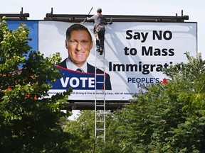 A worker removes a billboard featuring the portrait of People's Party of Canada (PPC) leader Maxime Bernier and its message "Say NO to Mass Immigration" in Toronto, August 26, 2019.  REUTERS/Moe Doiron