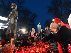 People lay symbolic sheaves of wheat and light candles during a commemoration ceremony at a monument to victims of the Holodomor famine of 1932-33 in Kiev on November 23, 2019
