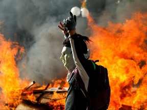A masked demonstrator gestures in front of a burning barricade during a protest at Providencia, a wealthy neighbourhood, in Santiago, Chile, on Wednesday, Nov. 6, 2019.