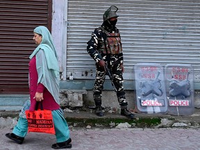 An Indian security personnel stands guard as a woman walks past during a lockdown in Srinagar on Nov. 5, 2019.