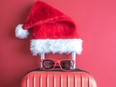 Flat lay of Santa Claus hat, sunglasses and luggage abstract isolated on red.