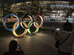 People take photographs of the Olympic Rings displayed in front of the New National Stadium, the main stadium for the upcoming Tokyo 2020 Olympic and Paralympic Games, at night on December 15, 2019 in Tokyo, Japan.