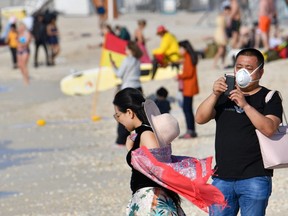 A tourist wearing a  mask takes pictures on a beach in the United Arab Emirates on Wednesday.