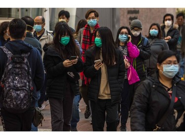 People wearing masks walk along a street in Hong Kong on January 30, 2020, as a preventative measure after a virus outbreak which began in the Chinese city of Wuhan. - Long queues outside of pharmacies and panic buying at supermarkets has become commonplace in Hong Kong in recent days as the crowded metropolis panics over the spread of China's new coronavirus. (Photo by DALE DE LA REY / AFP)