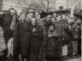 Holocaust survivors stand behind a barbed wire fence after the liberation of Nazi German death camp Auschwitz-Birkenau in 1945 in Nazi-occupied Poland, in this handout picture obtained by Reuters on Jan. 19, 2020. (Courtesy of Yad Vashem Archives)