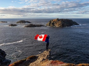 A woman holds a Canadian Flag looking out on the Atlantic Ocean, in Twillingate, Newfoundland and Labrador.