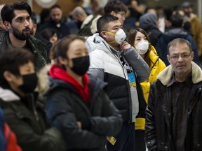 People wear masks as they wait for arrivals at  Pearson International Airport on Jan. 25, 2020. (The Canadian Press)