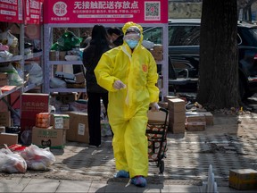 A resident, wearing full protective gear amid fears of the COVID-19 coronavirus, pulls a trolley after collecting packages from a drop-off stall for delivered goods outside a residential compound in Beijing on February 23, 2020.  NICOLAS ASFOURI/AFP via Getty Images)