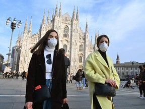 Women wearing a respiratory mask walk across Piazza del Duomo in central Milan on February 23, 2020.
