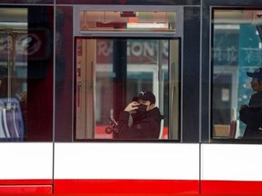 A man, wearing a mask, rides the street car through the Chinatown district of downtown Toronto, Ontario.