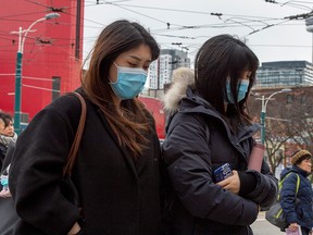 Pedestrians wear protective masks as they walk in Toronto on Monday, Jan. 27, 2020.