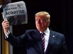 U.S. President Donald Trump holds up a copy of USA Today that displays the headline "Aquitted" as he arrives to speak at the 68th annual National Prayer Breakfast in Washington, D.C., on Thursday, Feb. 6, 2020.
