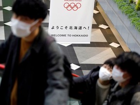 Passengers wearing protective face masks, following an outbreak of the coronavirus, are seen near a campaign banner for Tokyo 2020 Olympic Games at New Chitose Airport in Chitose, Hokkaido, northern Japan February 27, 2020.
